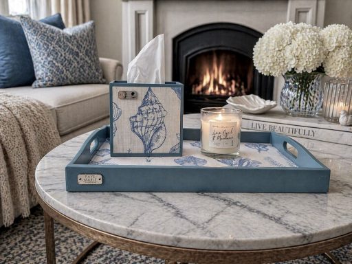 Coastal-inspired blue tray and matching tissue box with shell illustrations displayed on a marble coffee table, styled with candles